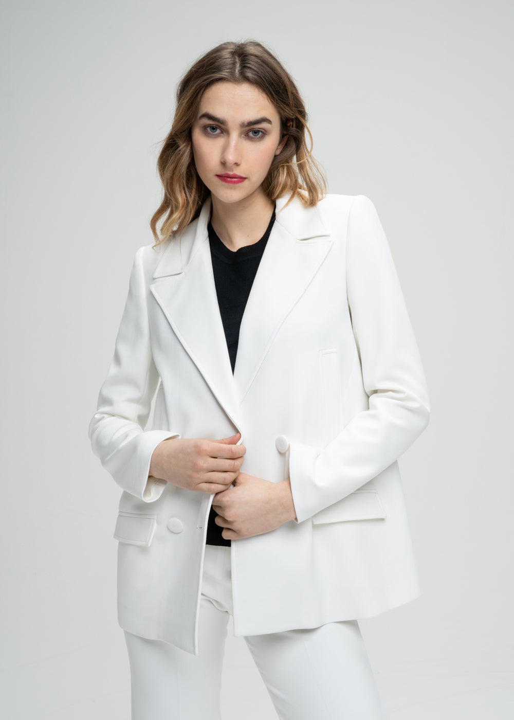 Gros plan sur un modèle portant un manteau caban blanc à coupe droite pour une allure subtilement surdimensionnée. Doté d’un double boutonnage croisé, de poches passepoilées et de poches à rabat fonctionnelles. Le logo sur chaque élément ajoute une touche personnalisée et raffinée à ce modèle élégant.