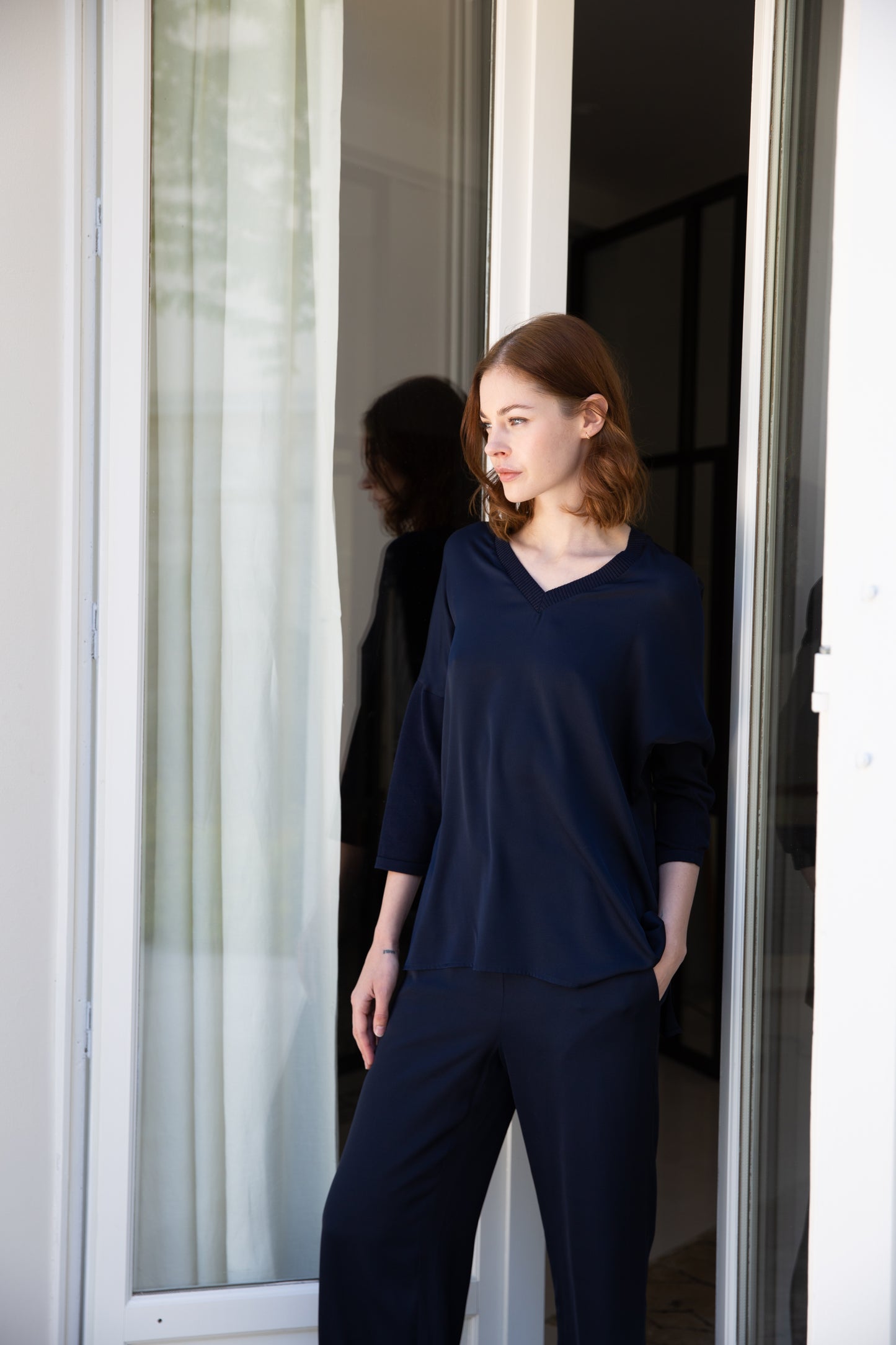 Modèle portant une tunique bi-matière jersey marin, élégante et au look distingué, offrant un effet texturé qui sublime la silhouette. Dotée de manches en jersey côtelé, d’un col côtelé et de fentes latérales, elle allie confort et sophistication.