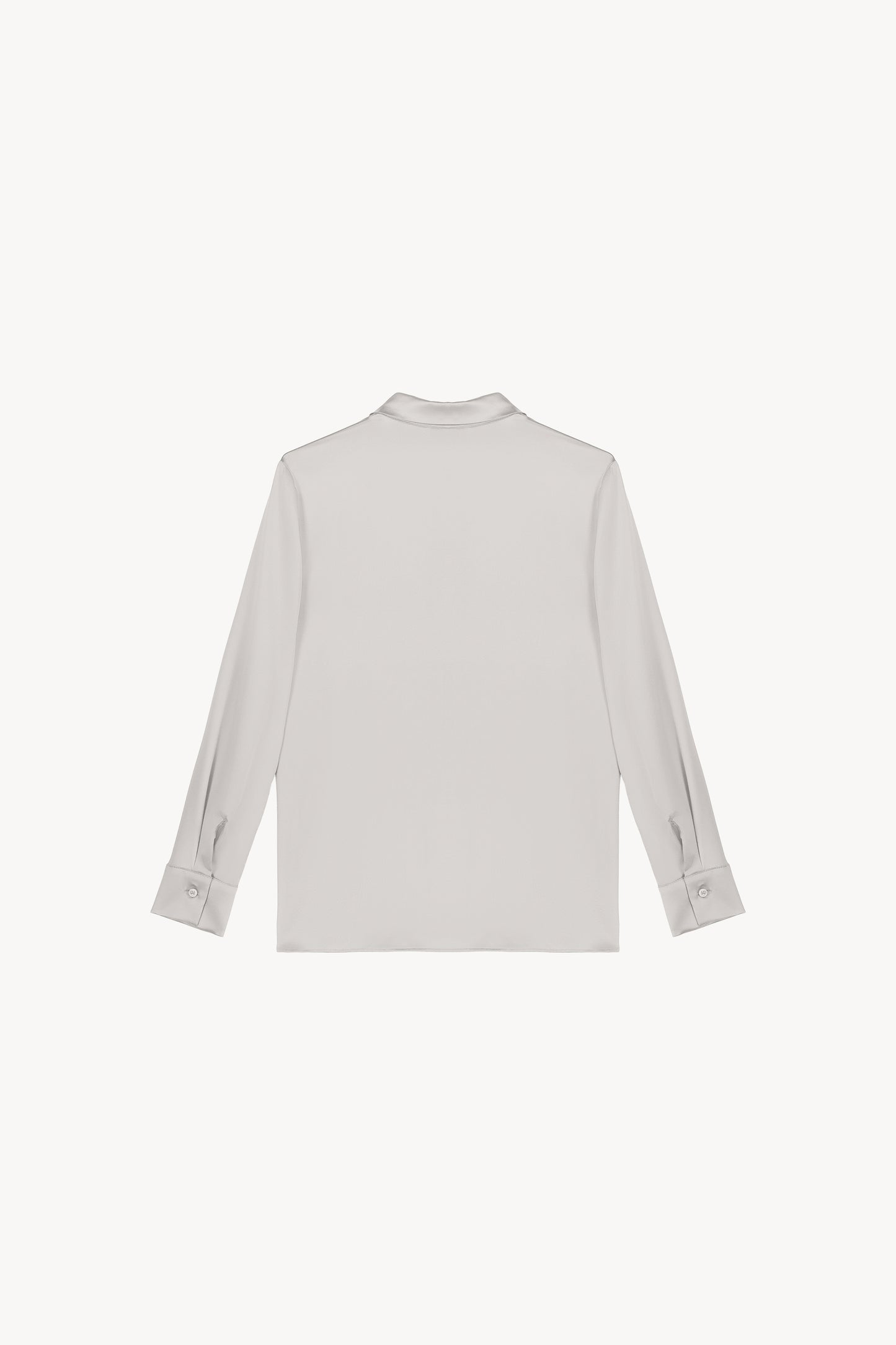 Chemise en satin de soie béton, lumineuse et éclatante, incarnant l'élégance ultime. Sa coupe fluide et son tissu soyeux sont sublimés par une patte de boutonnage cachée, des fentes latérales discrètes et un bas arrondi, créant une allure raffinée et sophistiquée.