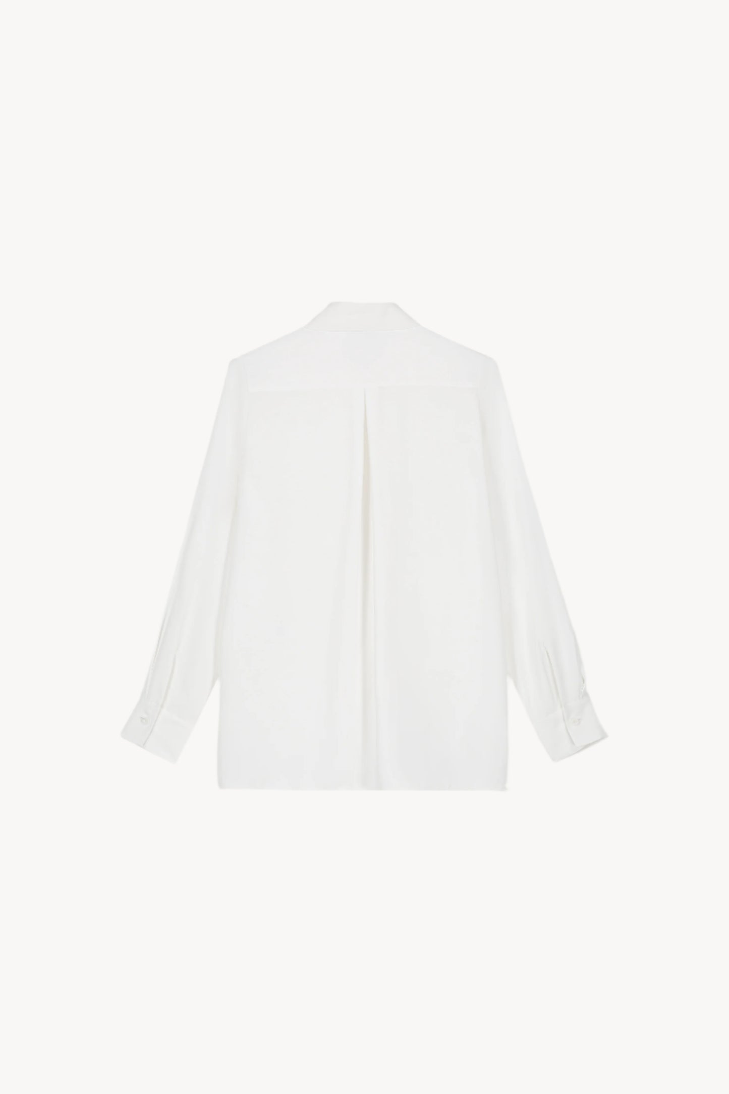 Chemise fluide à poche brodée blanc cassé sous un manteau, présentant une coupe classique, une poche plaquée à la poitrine et des fentes latérales.