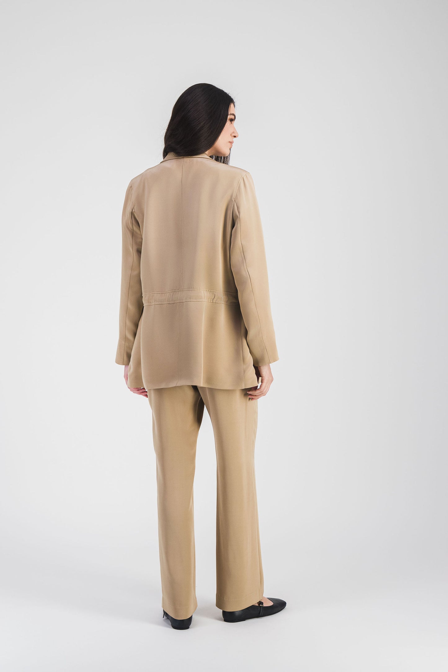 Veste saharienne beige en soie, col tailleur et cordon ajusté avec embouts métalliques gravés pour une allure chic.