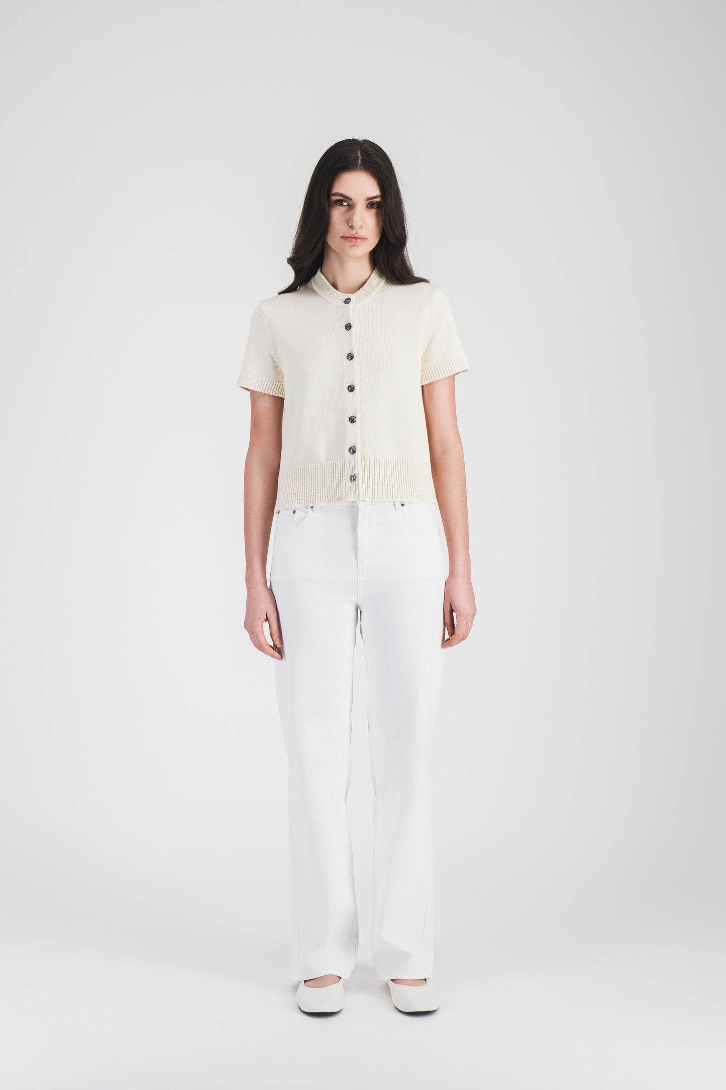 Gilet blanc cassé à manches courtes et finitions côtelées, orné de boutons en métal, pour un look élégant et minimaliste.