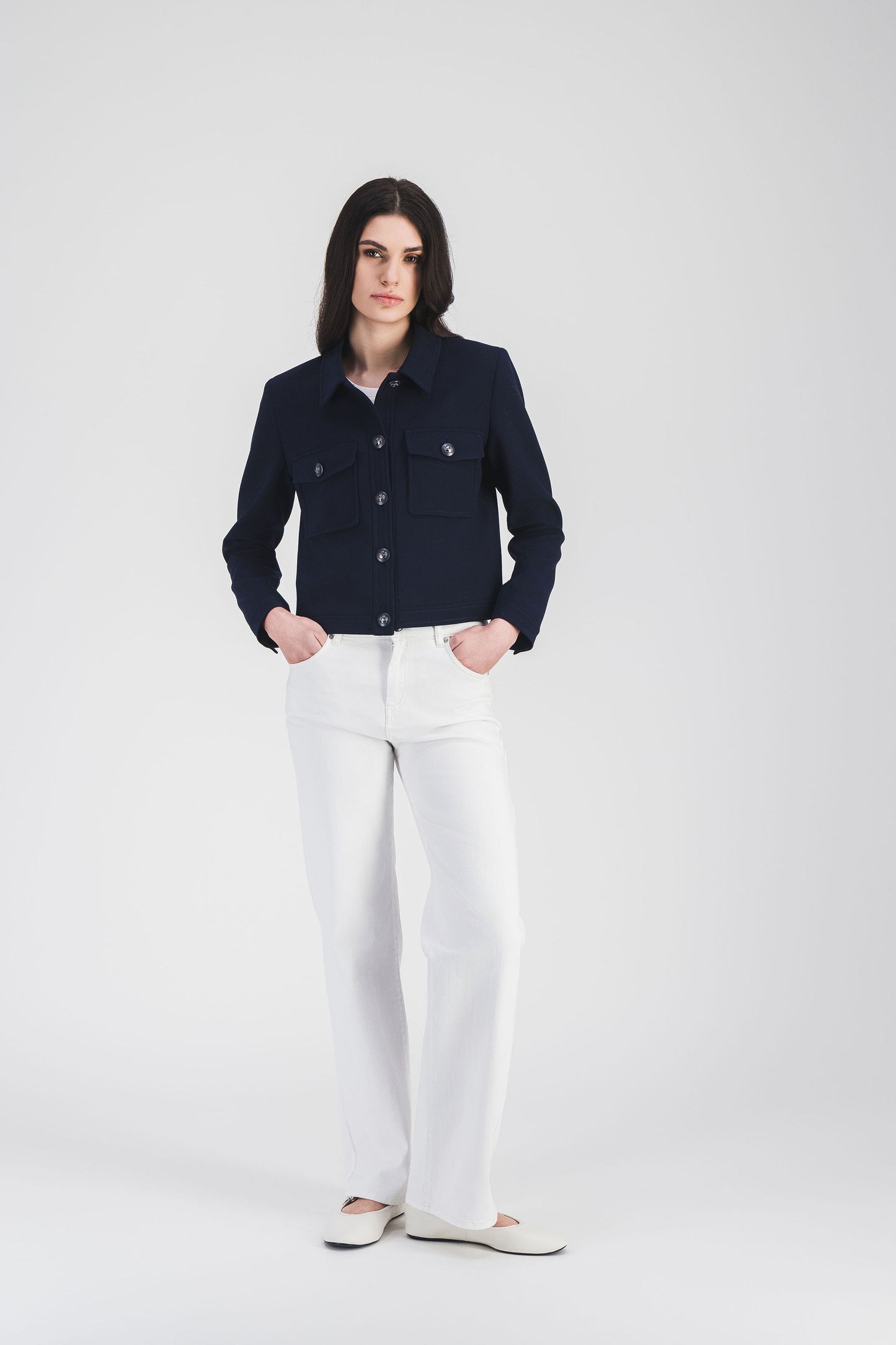 Élégante veste marine au col chemise intemporel, poches plaquées, bouton militaire et découpes structurées pour une silhouette moderne.