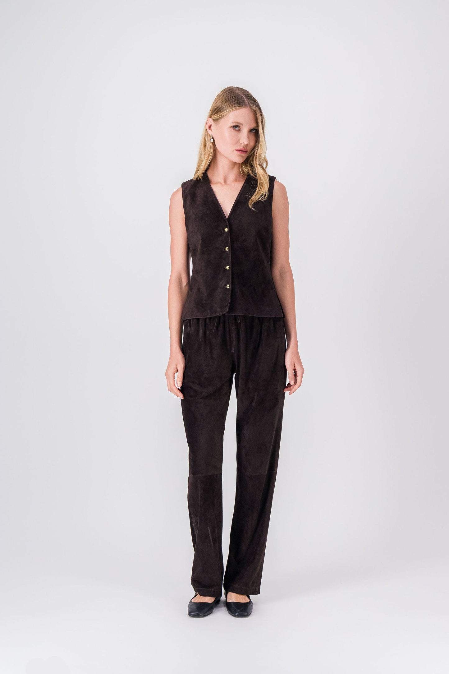 Gilet court en daim ébène, coupe ajustée avec surpiqûres discrètes et boutons dorés.