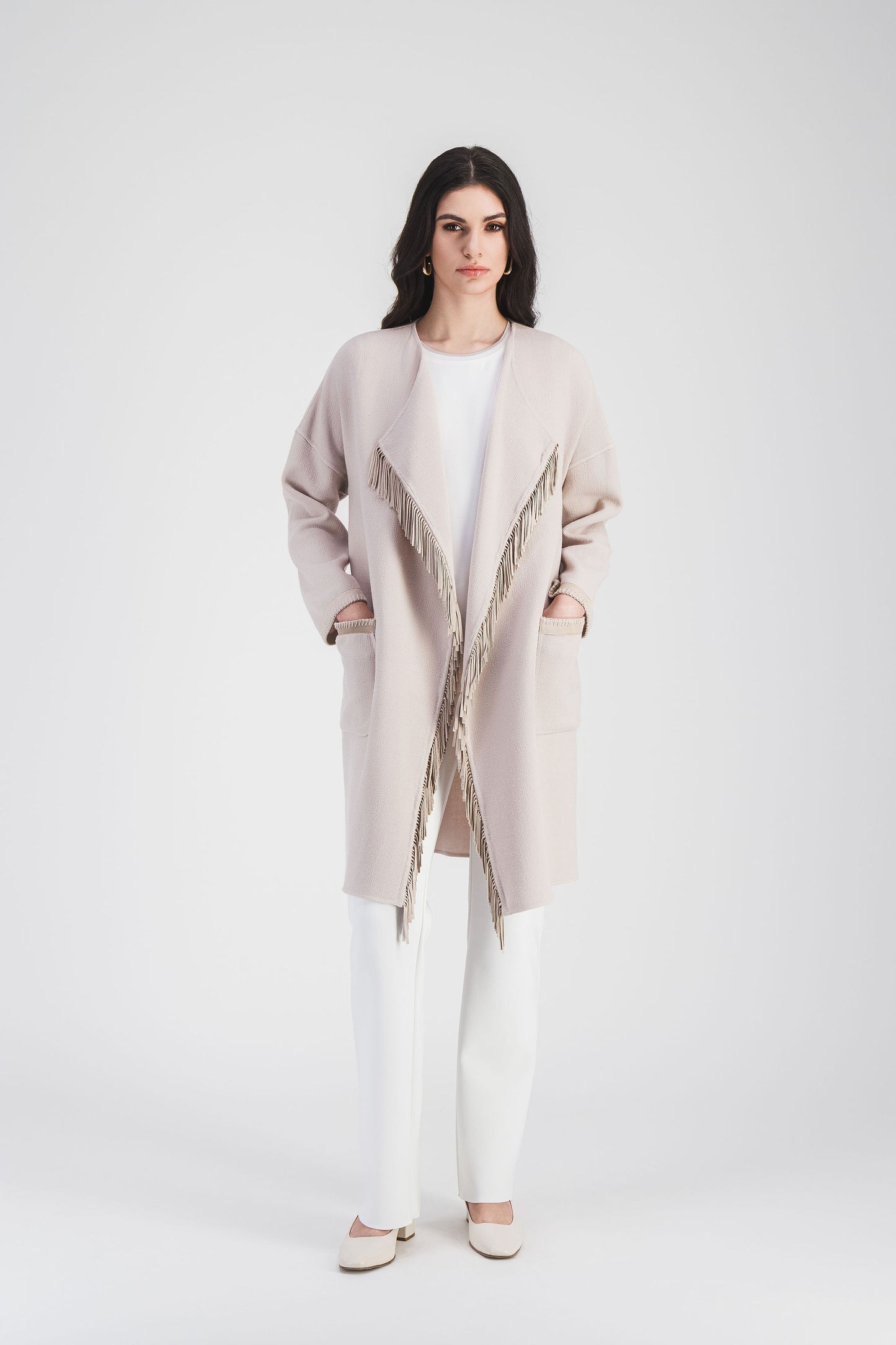 Manteau long mi-cuisse couleur béton avec franges en daim et coupe structurée, une pièce audacieuse.