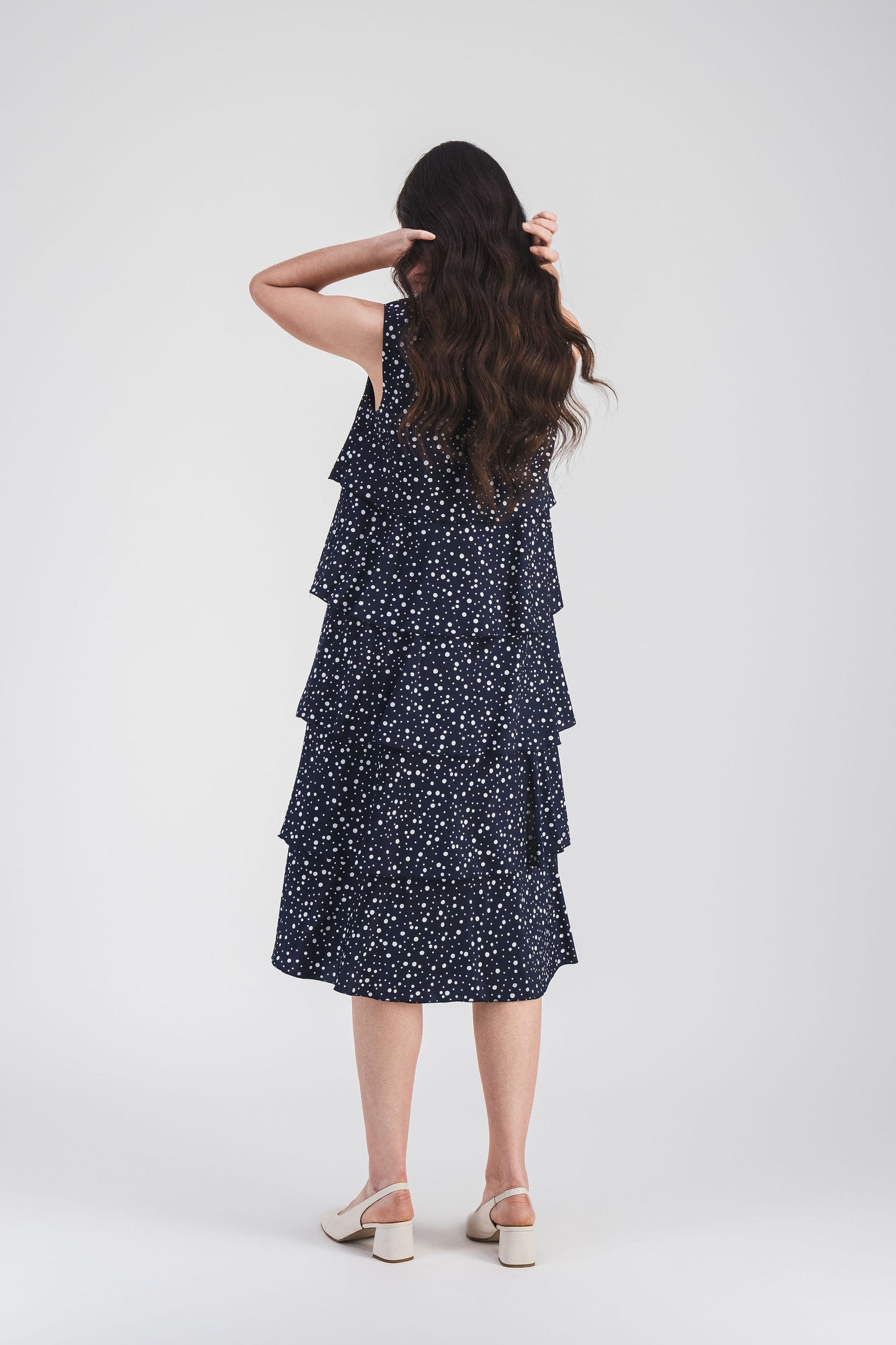 Robe marine à pois avec volants superposés et bouton dans le dos, offrant une coupe fluide et une allure élégante et raffinée.