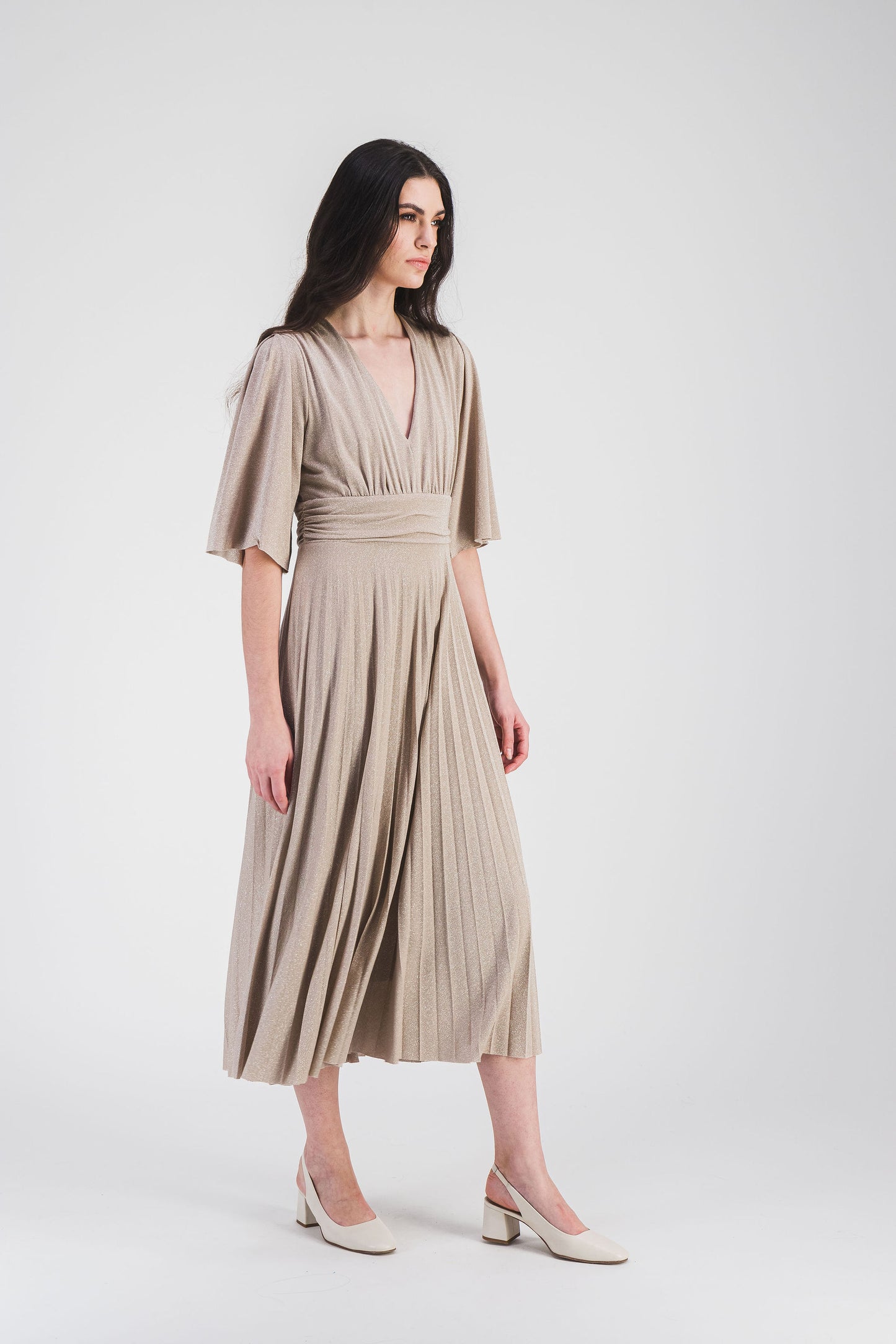 Robe longue cintrée avec col V, manches volantées et tissu scintillant. Le plissé soleil ajoute du mouvement et de l’élégance