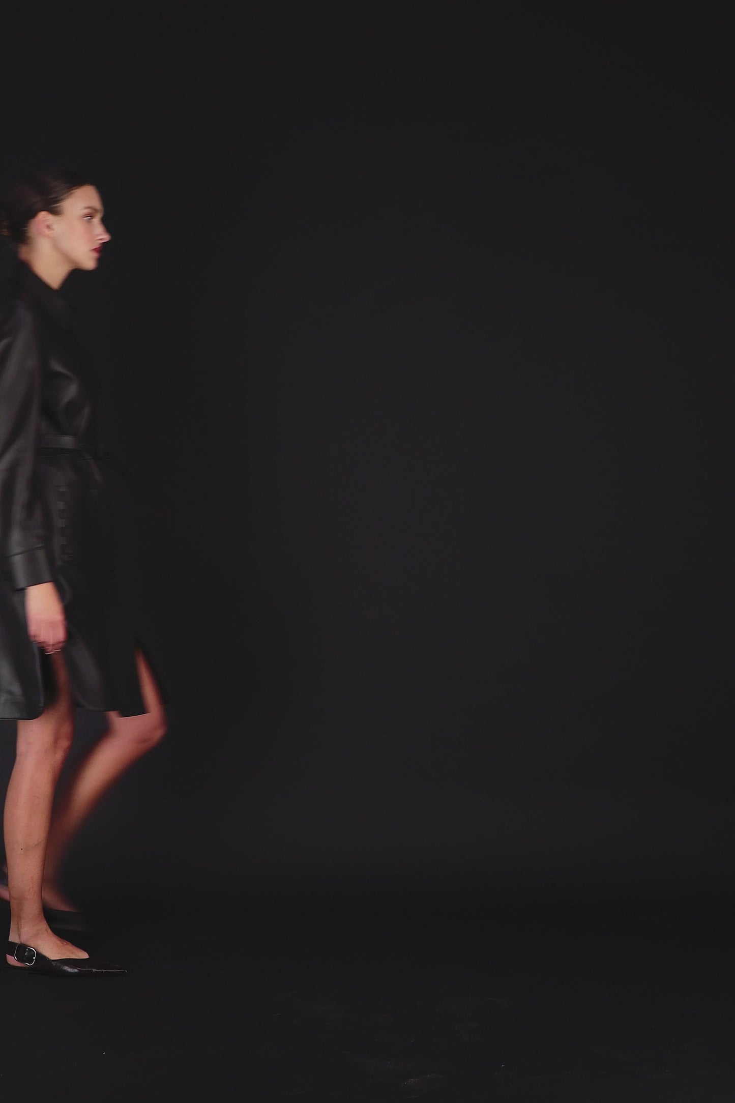 Vidéo d'un modèle portant un manteau en cuir orné de col chemise, fentes latérales, manches longues et deux poches.
