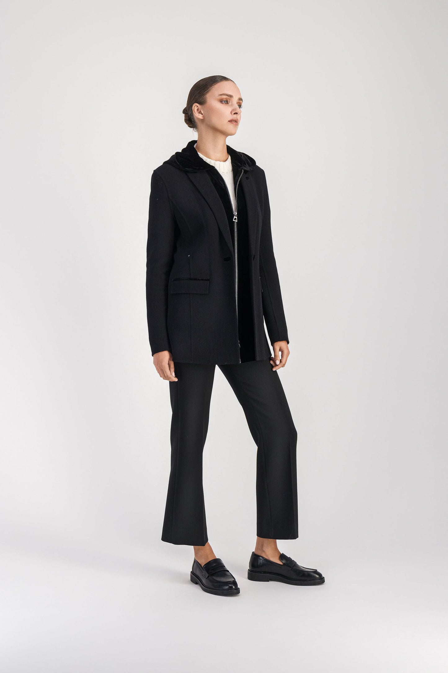 Modèle en position 3/4 portant un blazer trompe-l'œil noir présentant un style classique avec une capuche intégrée amovible, un col tailleur en velours, des poches plaquées et des détails en velours.