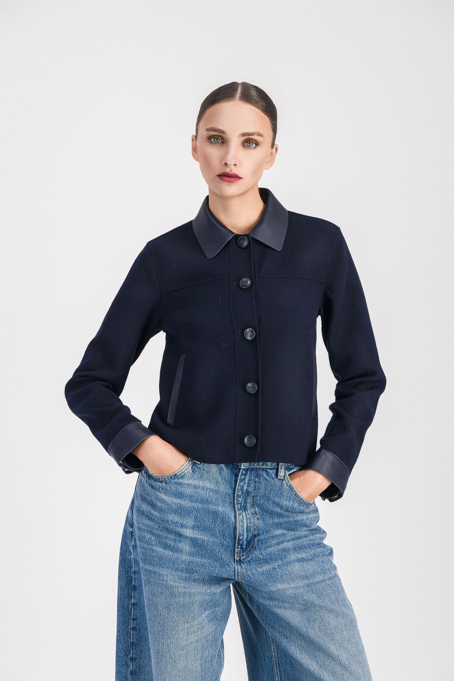 Gros plan sur un modèle portant une veste chemise ornée de détails en cuir est la pièce idéale pour adopter un look à la fois élégant et décontracté. Dotée d'un col chemise en cuir, d'une patte de boutonnage apparente, et d'un effet bi-matière, elle se distingue par ses boutons au logo Apostrophe, ses poches italiennes avant et ses manches en cuir.