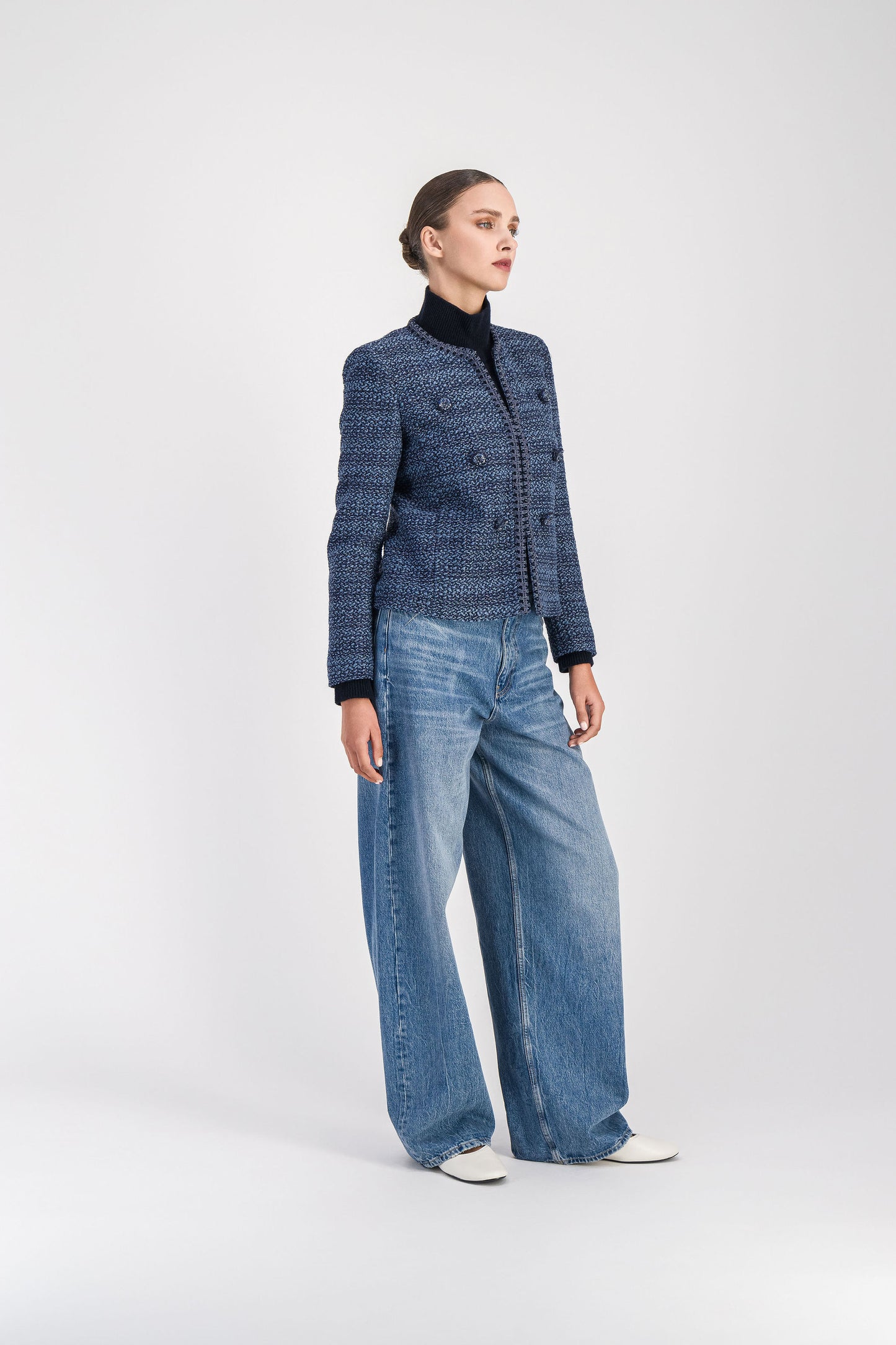 Modèle en position 3/4 portant une veste courte en tweed bleu denim présentant une coupe structurée, un col arrondi, des bordures tressées, un boutonnage apparent et des poches italiennes.