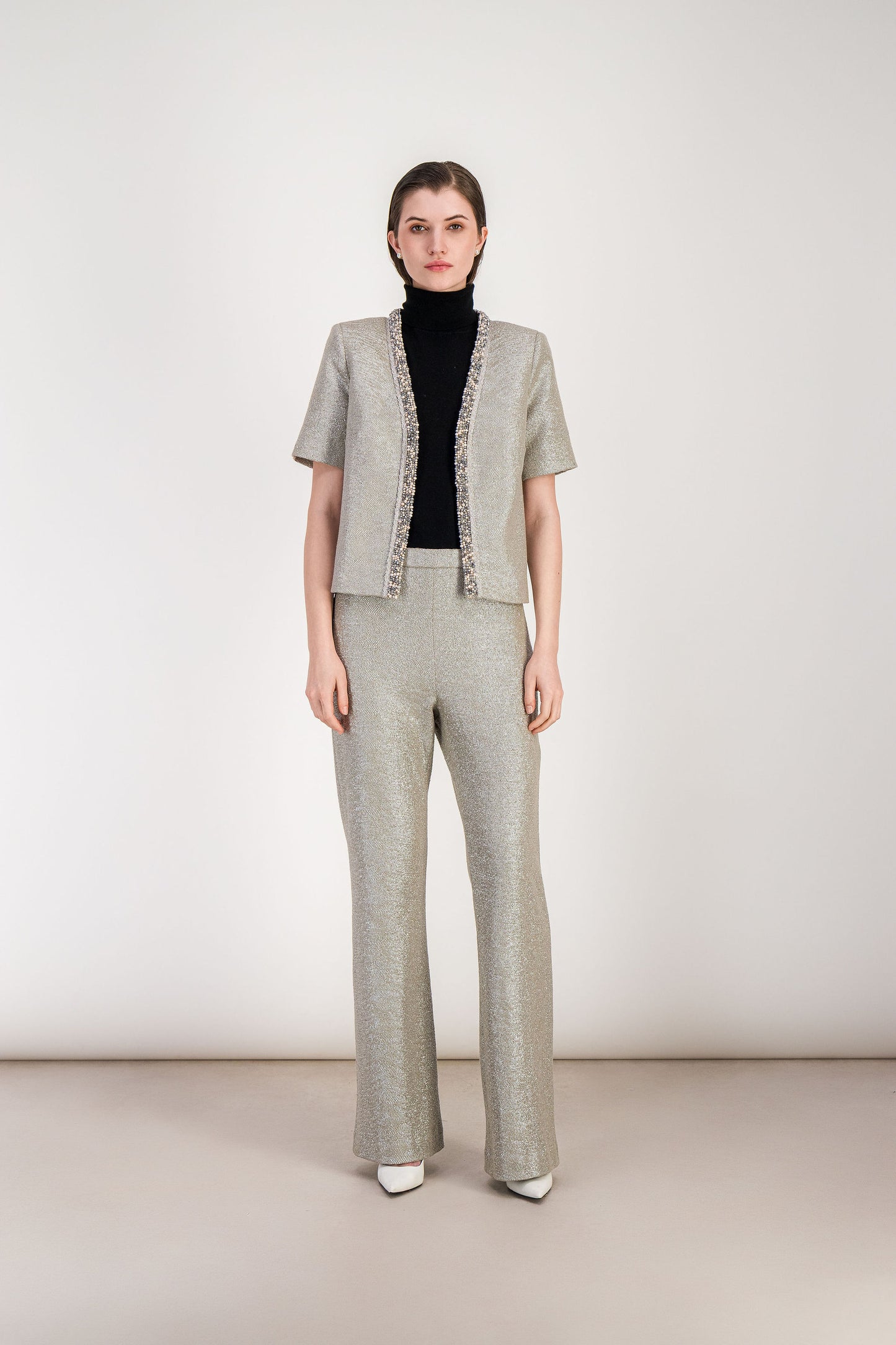 Veste droite en jersey lamé argent avec encolure en V soulignée d’un bord brodé.