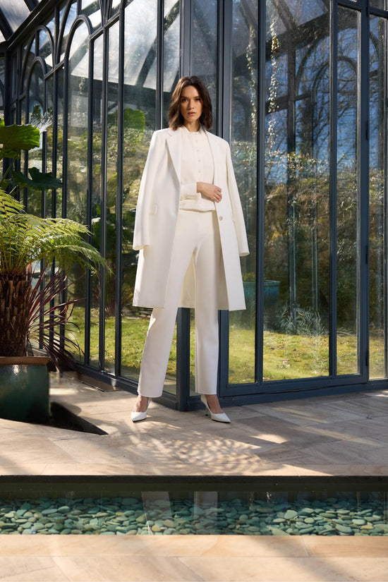 Manteau long et chic en blanc, avec trois boutons délicats et des poches passepoilées.