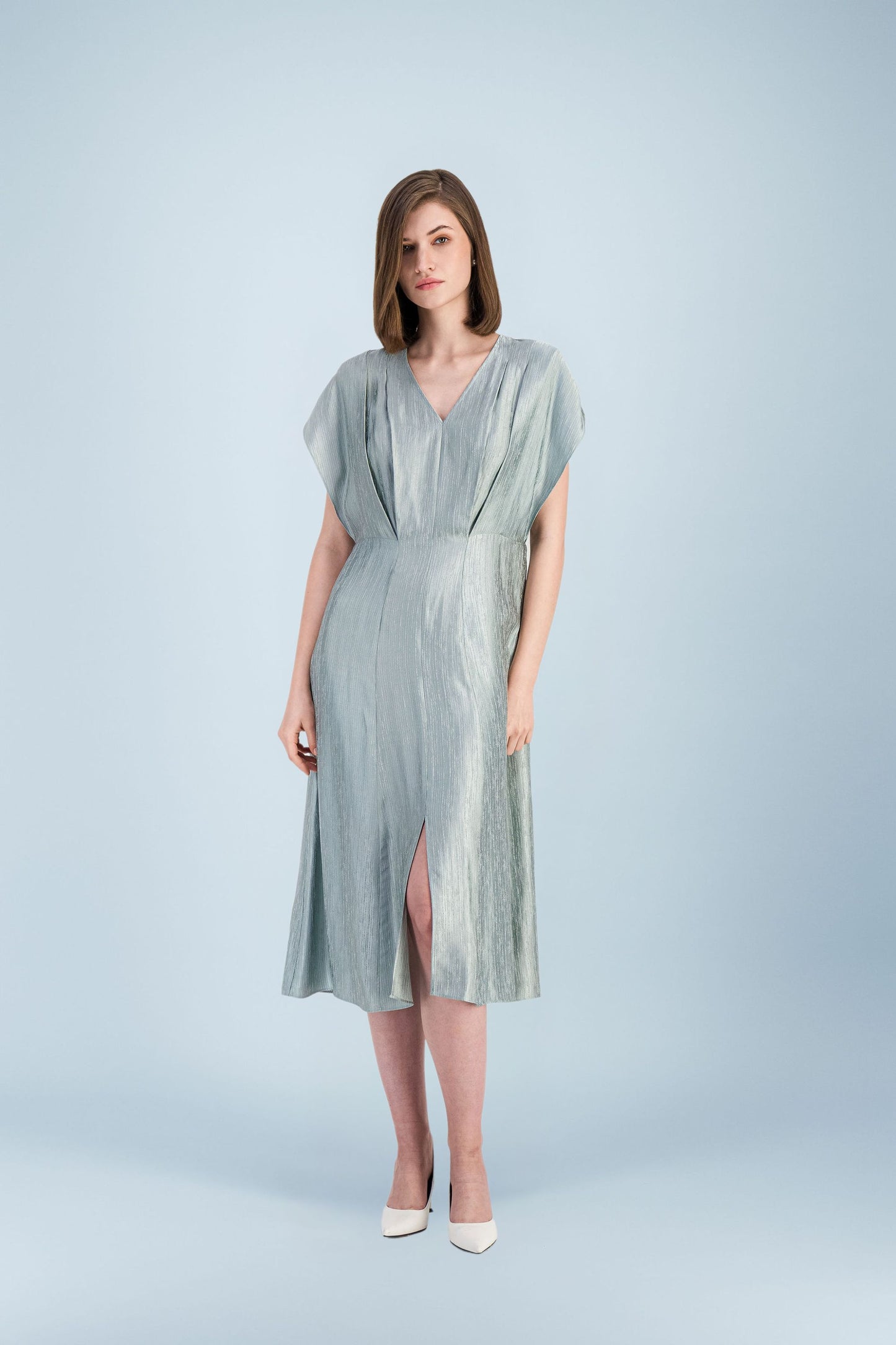Mannequin portant une robe midi vert clair à effet satiné, avec encolure en V, manches courtes et fente sur le devant, associée à des escarpins blancs.