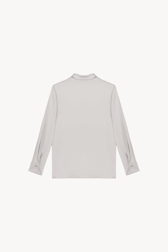 Chemise en satin de soie béton, lumineuse et éclatante, incarnant l'élégance ultime. Sa coupe fluide et son tissu soyeux sont sublimés par une patte de boutonnage cachée, des fentes latérales discrètes et un bas arrondi, créant une allure raffinée et sophistiquée.