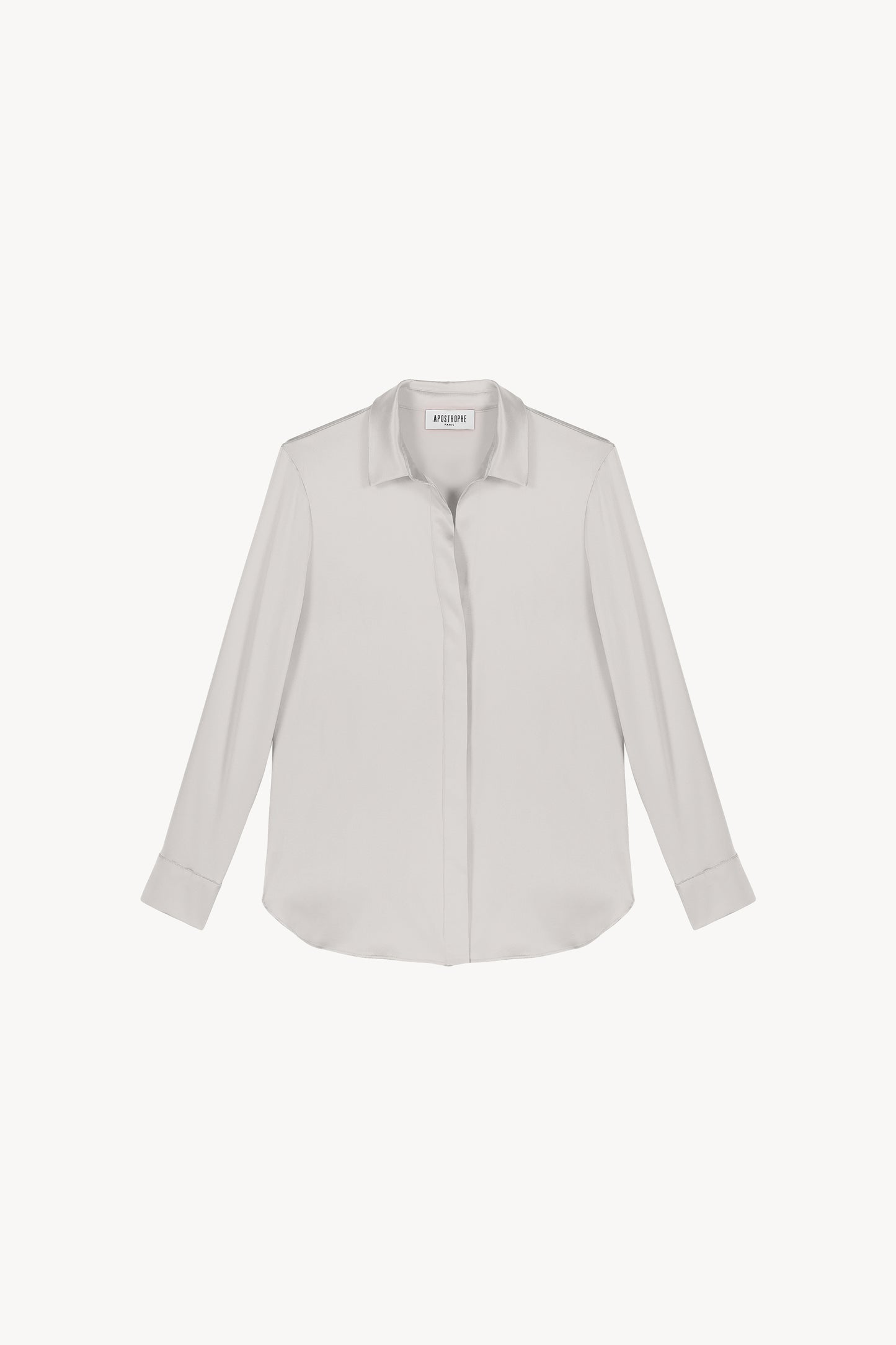 Chemise en satin de soie béton, lumineuse et éclatante, incarnant l'élégance ultime. Sa coupe fluide et son tissu soyeux sont sublimés par une patte de boutonnage cachée, des fentes latérales discrètes et un bas arrondi, créant une allure raffinée et sophistiquée.
