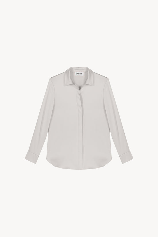Chemise en satin de soie béton, lumineuse et éclatante, incarnant l'élégance ultime. Sa coupe fluide et son tissu soyeux sont sublimés par une patte de boutonnage cachée, des fentes latérales discrètes et un bas arrondi, créant une allure raffinée et sophistiquée.