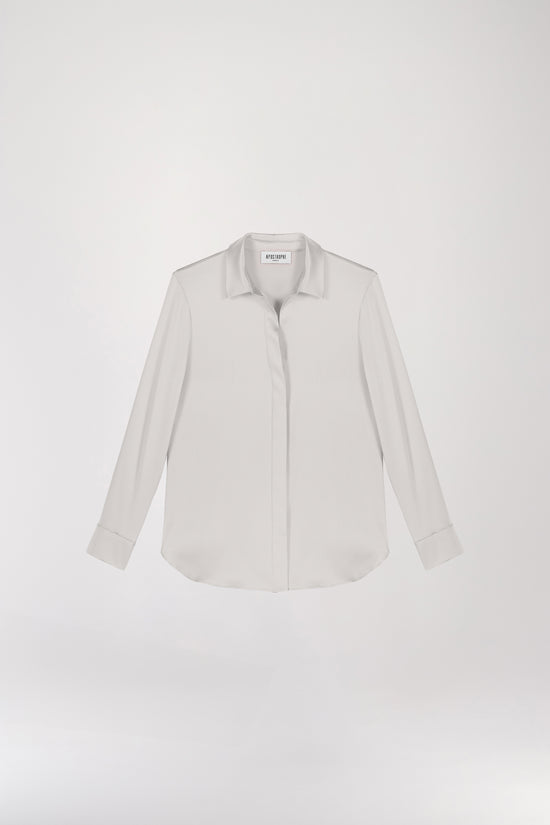 Chemise en satin de soie béton, lumineuse et éclatante, incarnant l'élégance ultime. Sa coupe fluide et son tissu soyeux sont sublimés par une patte de boutonnage cachée, des fentes latérales discrètes et un bas arrondi, créant une allure raffinée et sophistiquée.