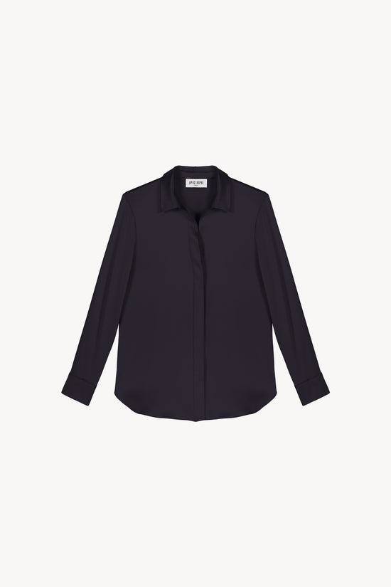 Chemise en satin de soie marine, resplendissante et rayonnante, incarnant l'élégance absolue. Sa coupe fluide et son tissu soyeux offrent une texture luxueuse, sublimée par une patte de boutonnage dissimulée, des fentes latérales discrètes et un ourlet arrondi en bas.