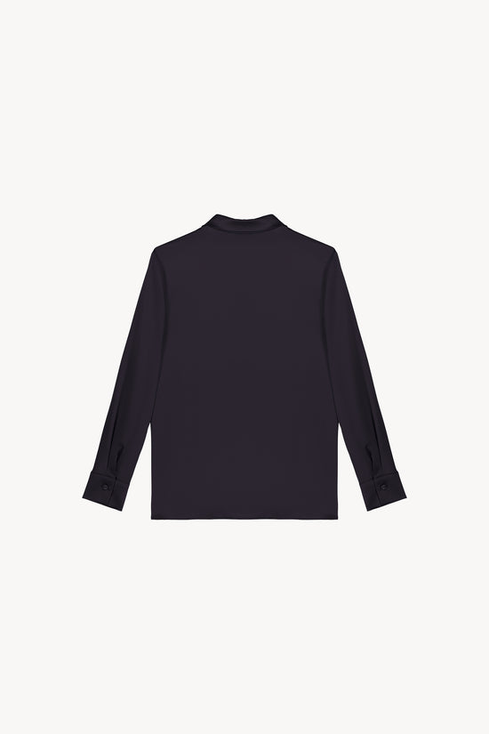 Chemise en satin de soie marine, resplendissante et rayonnante, incarnant l'élégance absolue. Sa coupe fluide et son tissu soyeux offrent une texture luxueuse, sublimée par une patte de boutonnage dissimulée, des fentes latérales discrètes et un ourlet arrondi en bas.