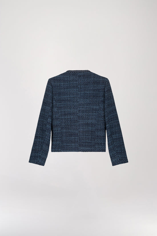 Veste courte en tweed bleu denim présentant une coupe structurée, un col arrondi, des bordures tressées, un boutonnage apparent et des poches italiennes.