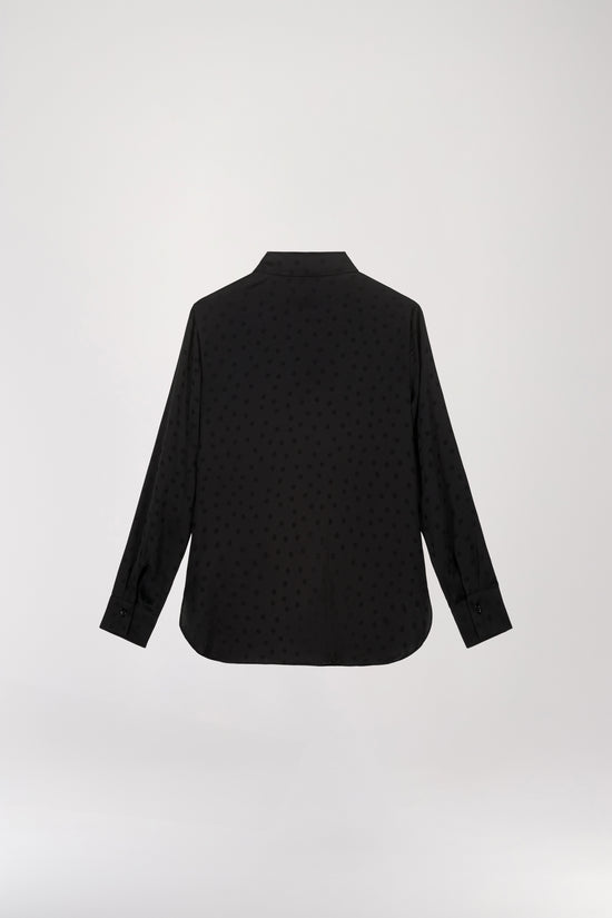 Chemise en soie à pois noire, présentant une coupe fluide, un col chemise, une patte de boutonnage cachée et des boutons nacrés aux poignets.