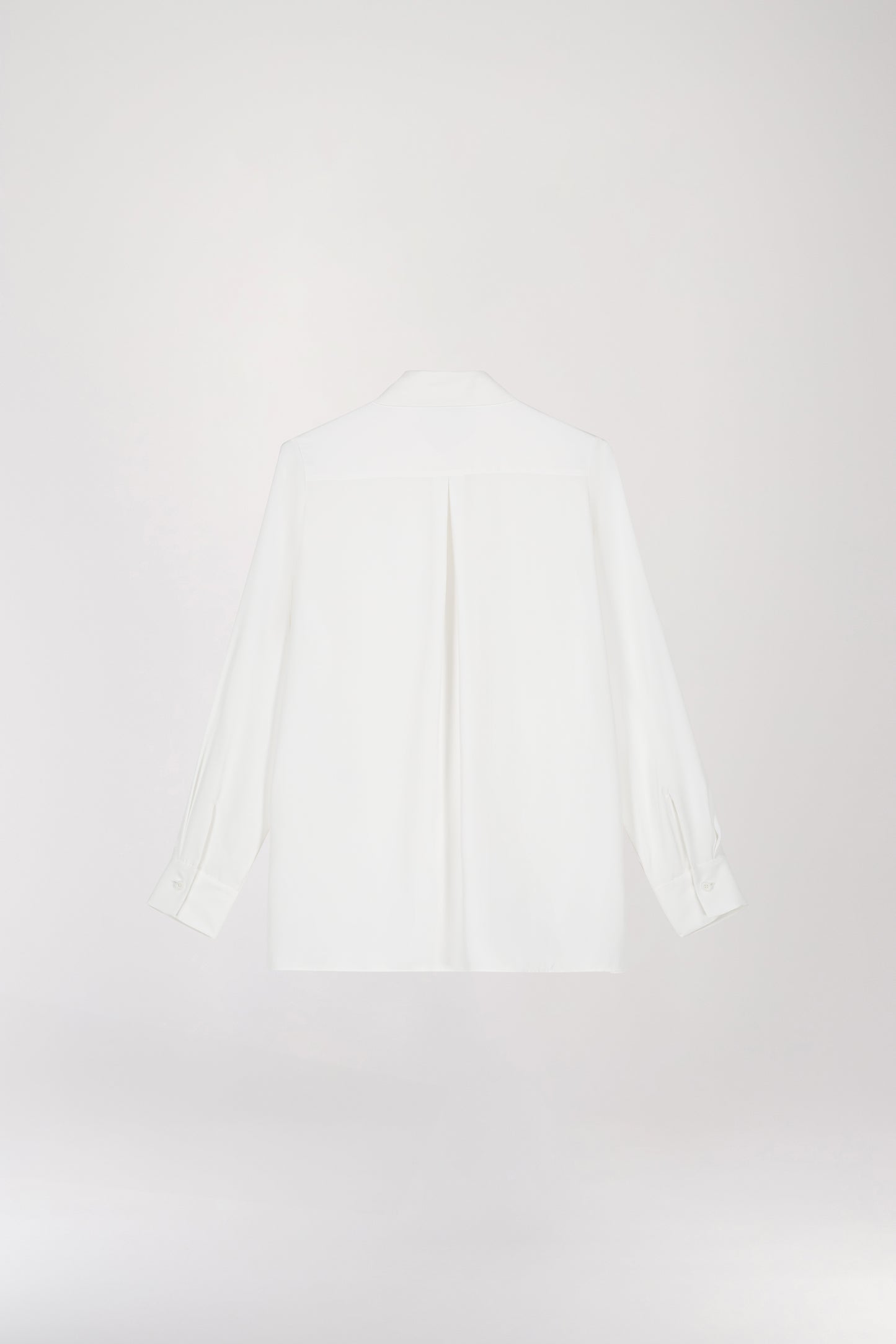 Chemise fluide à poche brodée blanc cassé sous un manteau, présentant une coupe classique, une poche plaquée à la poitrine et des fentes latérales.