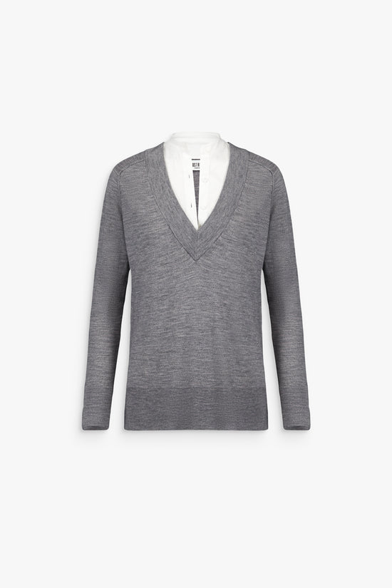 Femme portant un pull gris moyen trompe-l’œil, laissant apparaître une bande de popeline blanche au col.