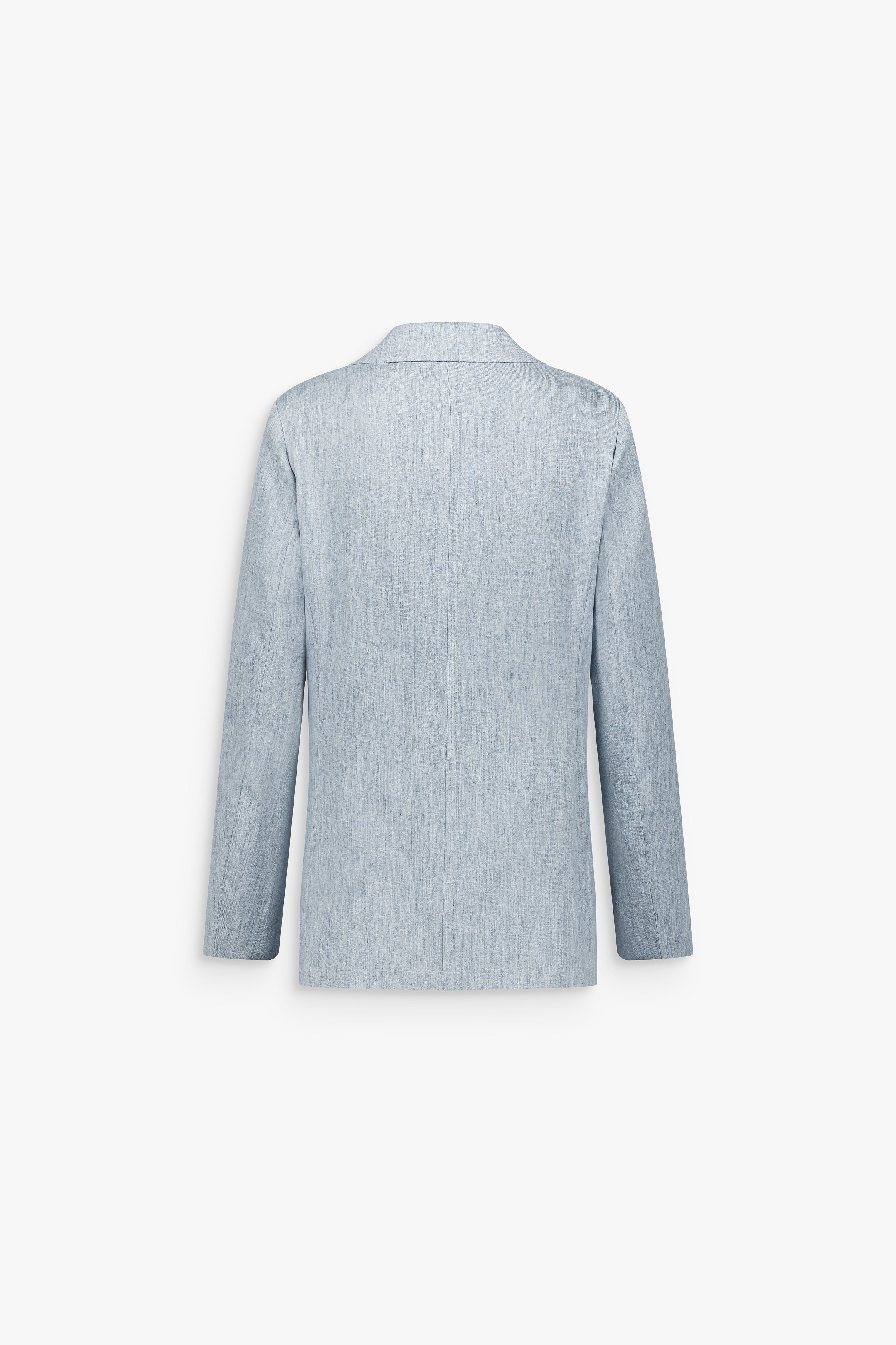 Détail d’une veste bleu denim à la coupe ajustée, révélant le grain naturel d’une matière en lin mélangé.