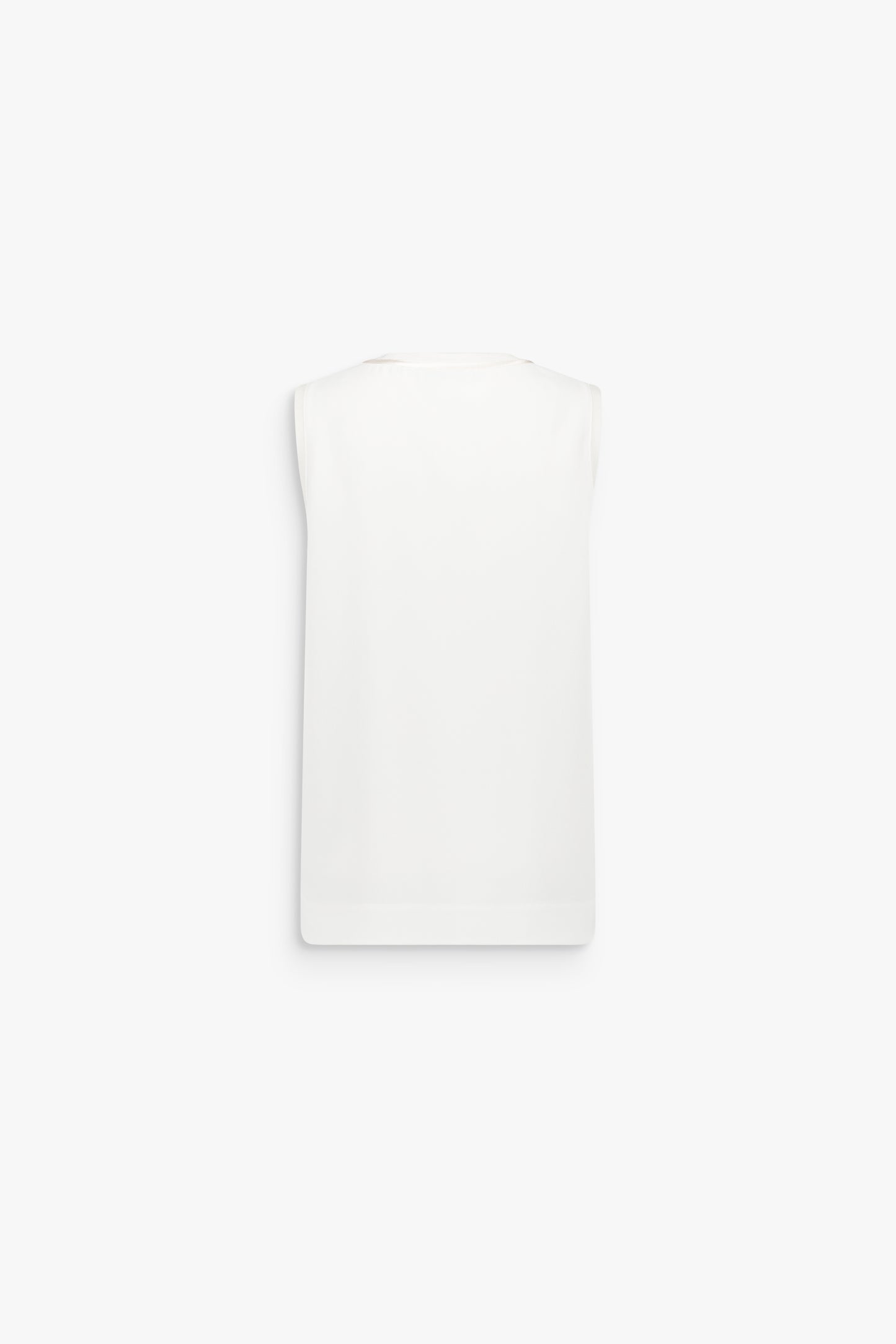 Détail d’un top blanc cassé à coupe ample, souligné par des finitions satinées discrètes.