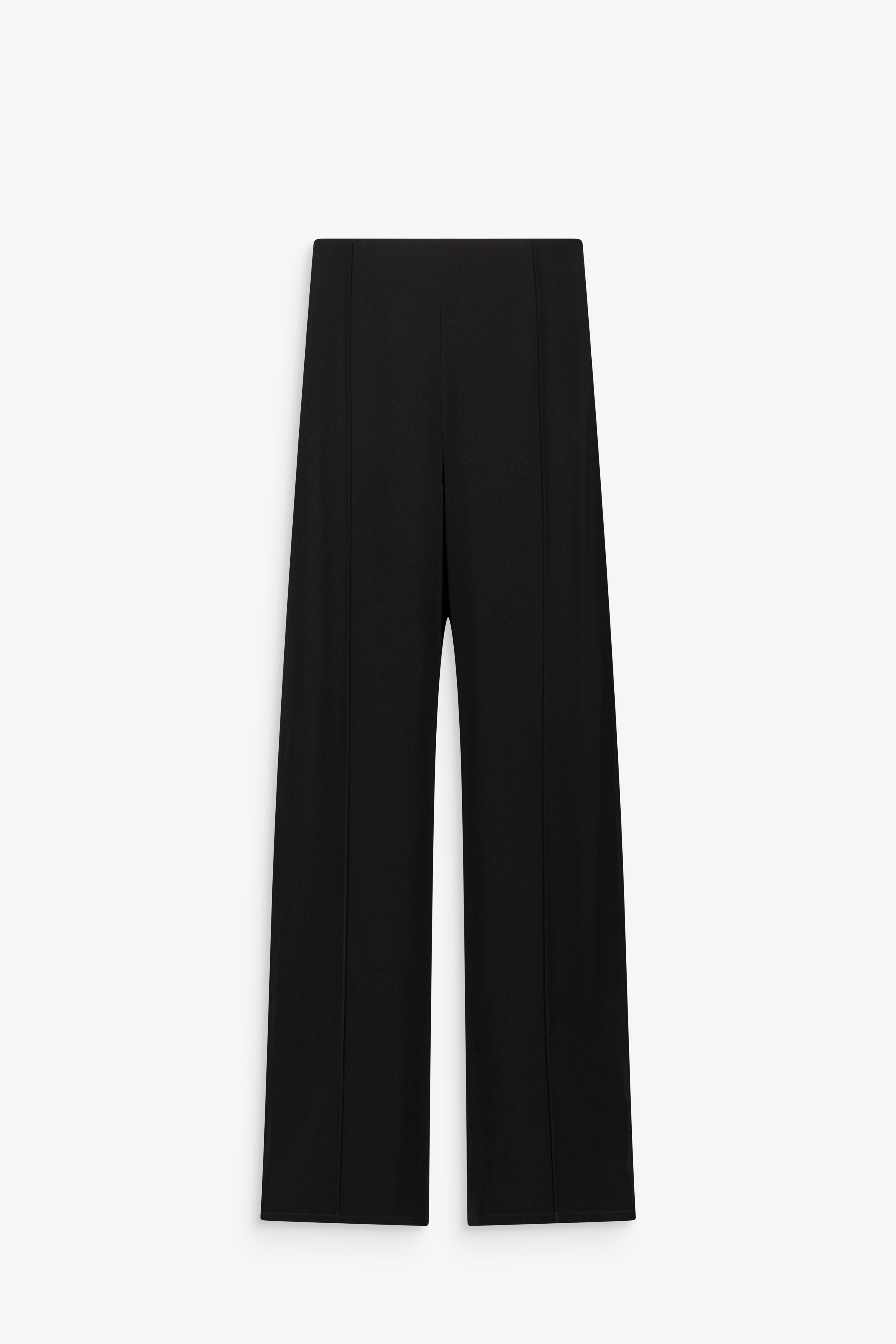 Pantalon noir à taille haute, coupe droite et plis centraux sur les jambes, avec fermeture zippée invisible sur le côté.
