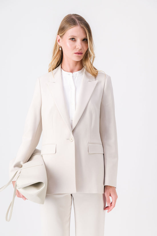Le col tailleur, la double boutonnière et les poches plaquées structurent la silhouette