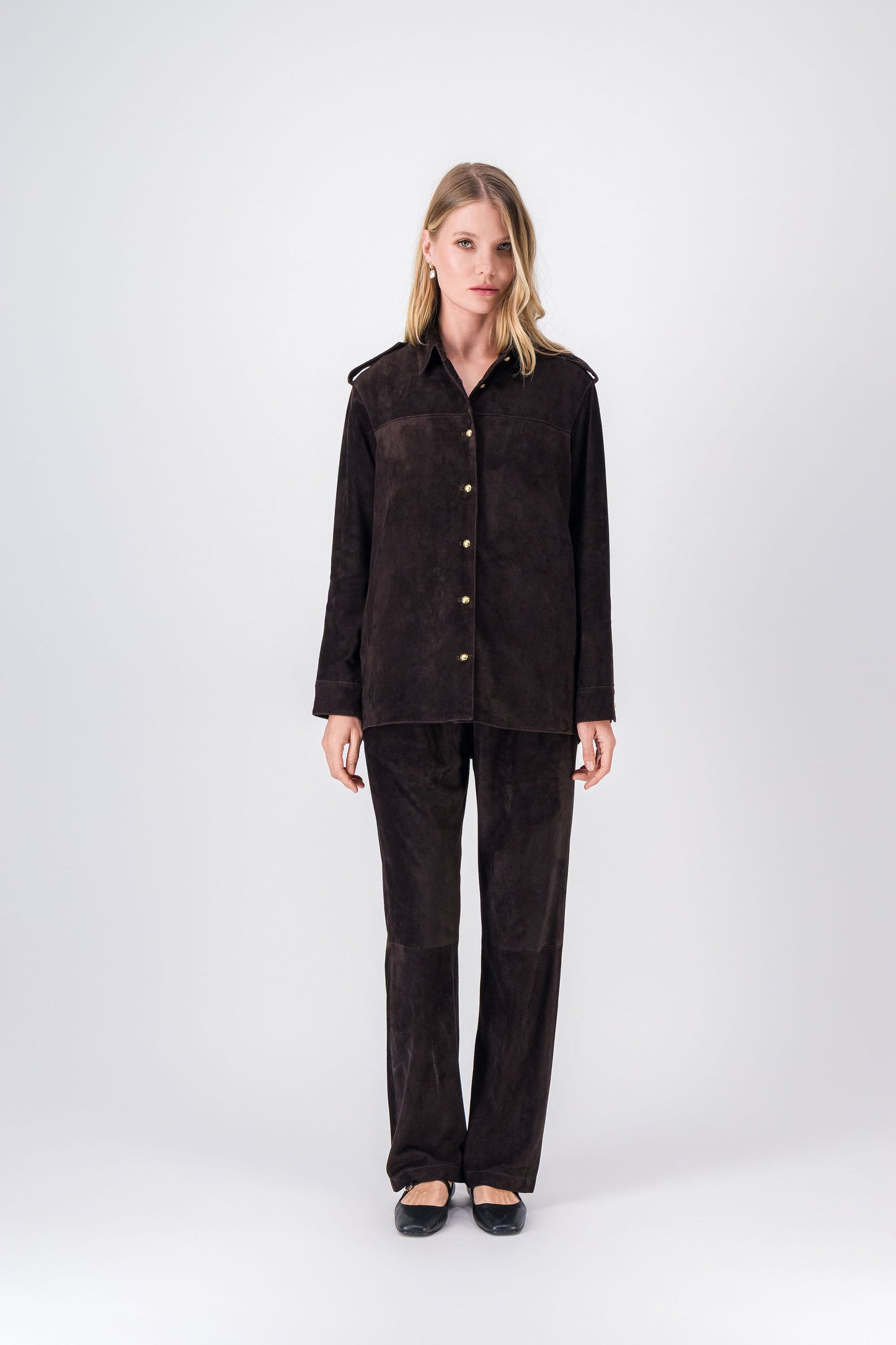 Blouson en daim ébène, coupe droite avec pattes d’épaule, col classique et boutons dorés.