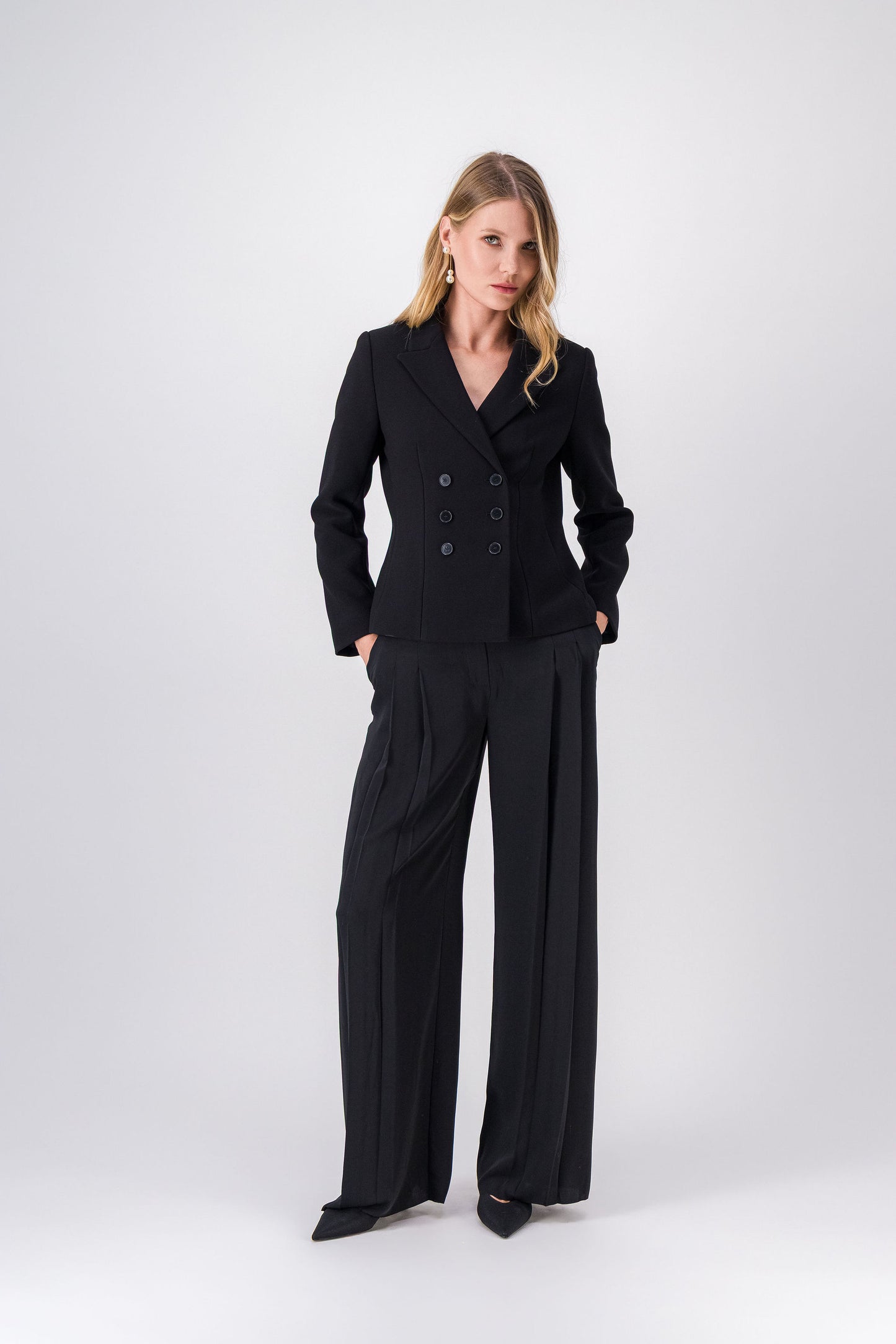 Pantalon noir coupe ample, deux plis, ceinture à passants et poches passepoilées.