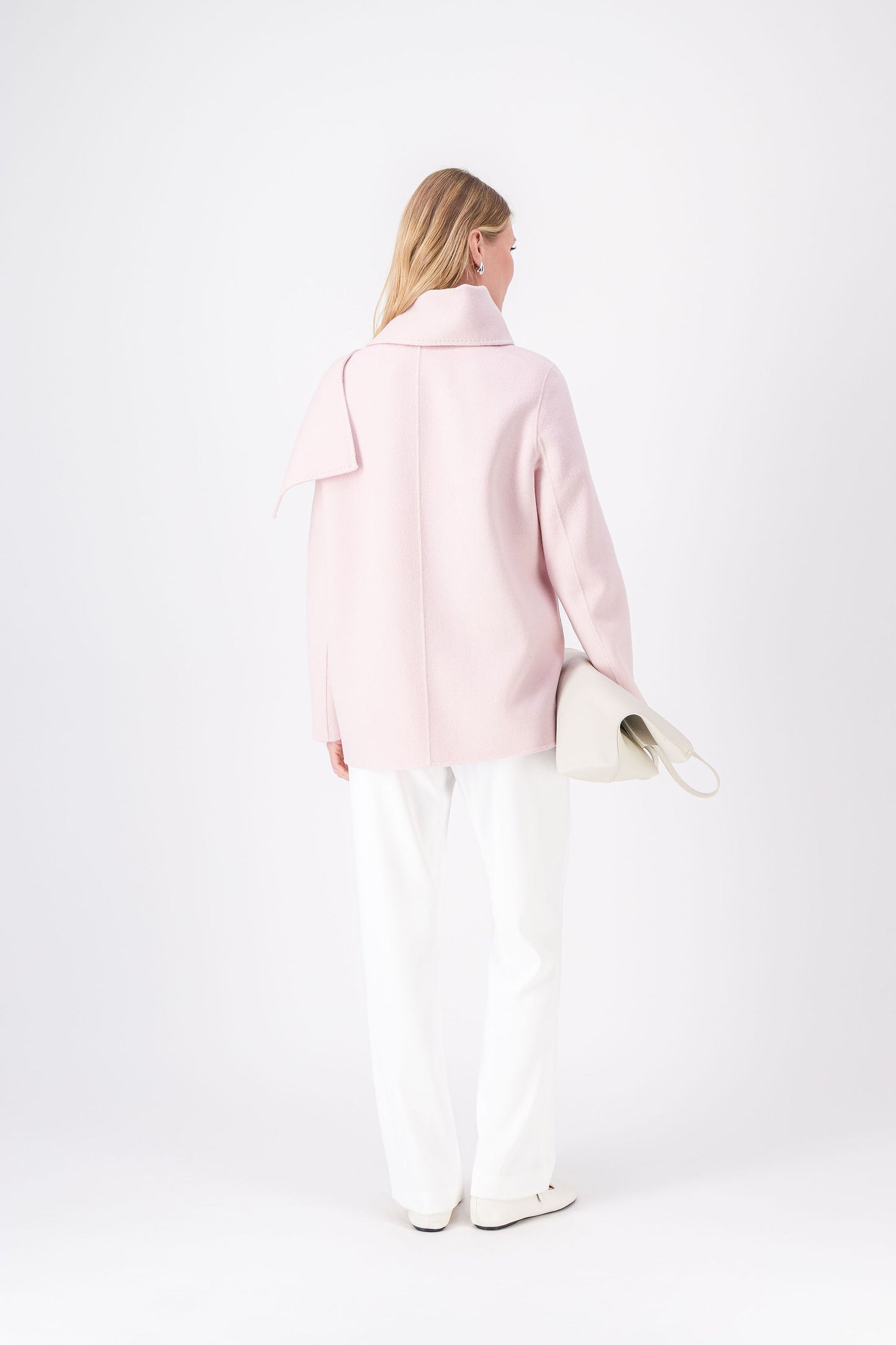 Détail des poches plaquées et de l’écharpe intégrée sur le manteau rose pâle.