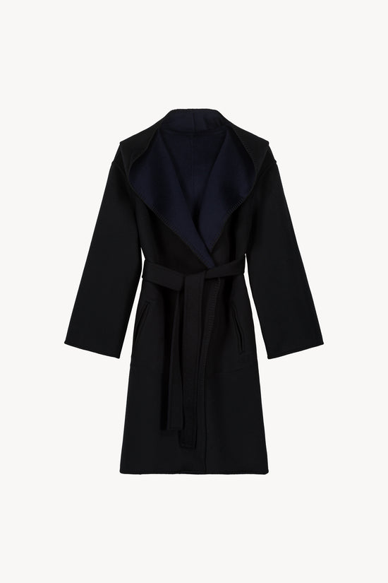 Manteau oversize réversible noir et marine. Col tailleur, capuche intégrée. Finitions à points feston faits main. Ceinture ton sur ton et poches plaquées sur chaque face.